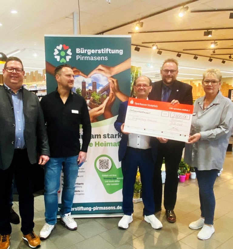 Eine Gruppe von sieben Personen steht im Edeka Kissel SBK in Pirmasens vor einem Banner der Bürgerstiftung Pirmasens. Auf diesem Bild wird eine großer Spendenscheck der Sparkasse Südpfalz über 2.800 Euro übergeben. Im Hintergrund sind frisches Obst und Gemüse sowie eine Feinkostabteilung zu sehen. Die Übergabe findet offenbar im Rahmen einer Spendenaktion zugunsten der Bürgerstiftung statt.
